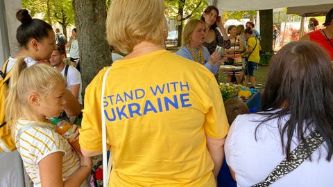 "Stand with Ukraine" (Solidarität mit der Ukraine) war auf dem T-Shirt einer Frau zu lesen, die ukrainischen Kindern dabei zusah, die an einem Stand Friedenstauben bastelten. (Foto: SWR, Foto: Maxim Flößer)