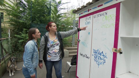 Eine Gedenktafel lässt Stuttgarter Obdachlose an Verstorbene erinnern. Laura zeigt Pfarrerin Stephanie Hecke, wohin sie den Namen ihres kürzlich verstorbenen Freundes Blacky geschrieben hat. (Foto: SWR)