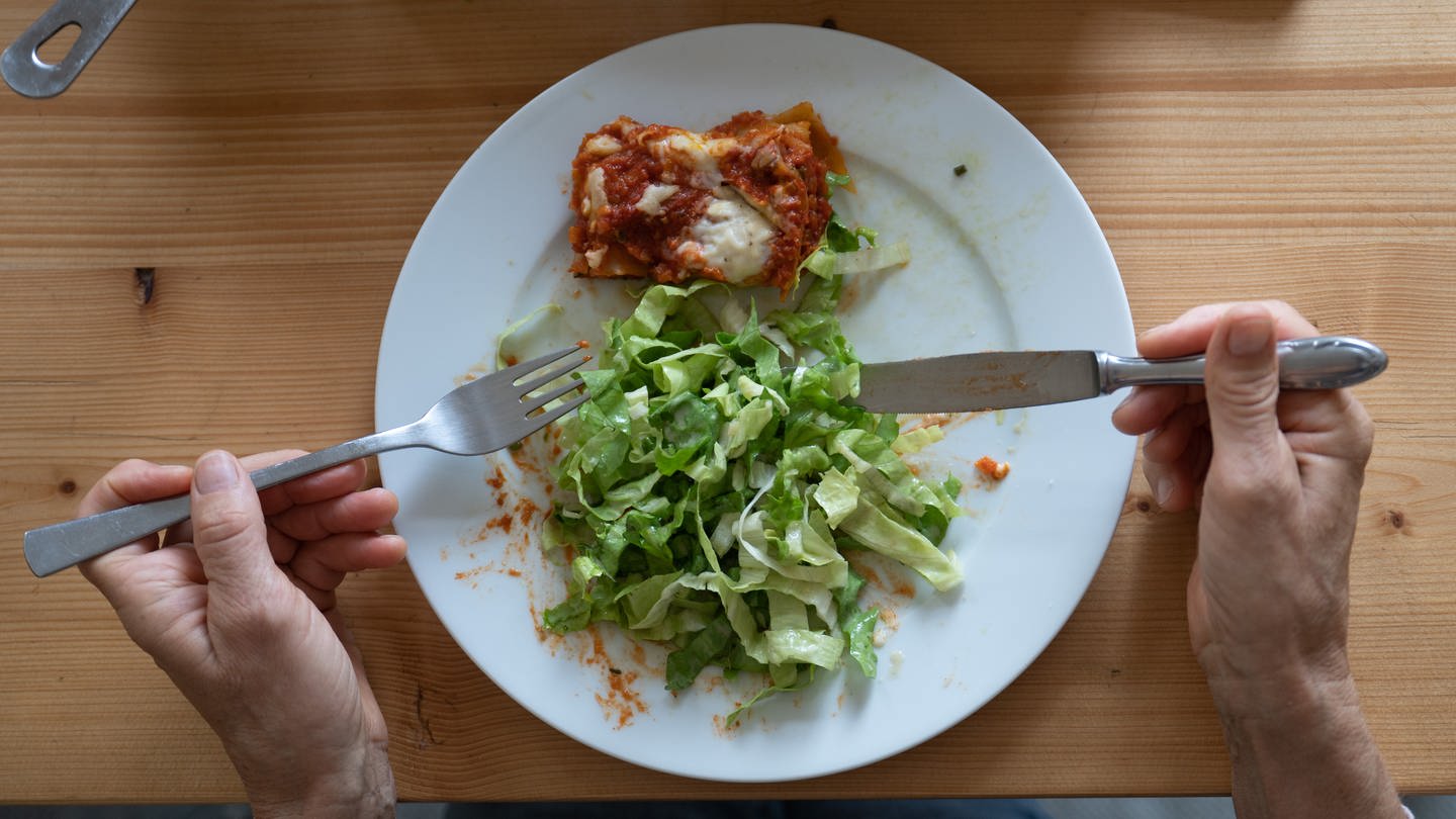 Eine Frau isst eine vegetarische Lasagne aus Linsen mit einem grünen Salat. Immer mittwochs gibt es in den Einrichtungen der Evangelischen Heimstiftung kein Fleisch mehr auf den Speiseplänen. Daran gibt es Kritik. (Foto: dpa Bildfunk, picture alliance/dpa | Sebastian Gollnow)