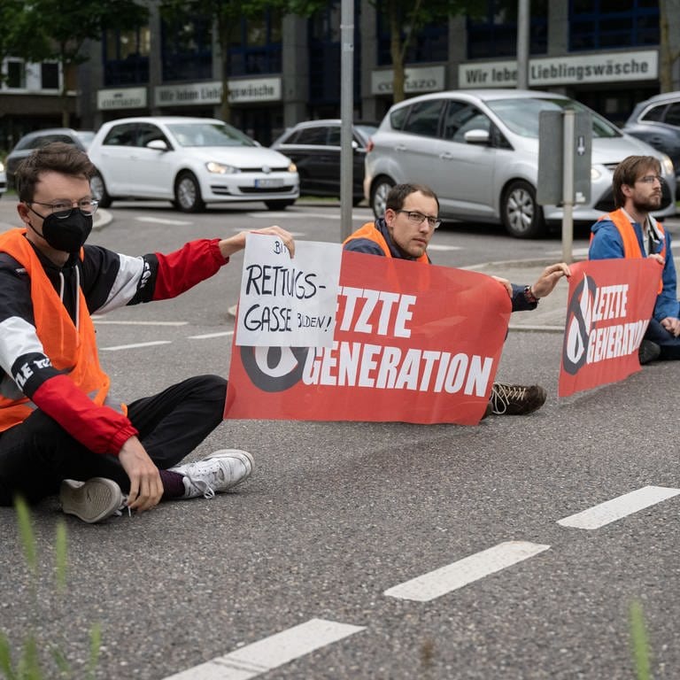 Drei Klimaaktivisten der Gruppe "Letzte Generation" blockieren eine Straße in Stuttgart.  (Foto: dpa Bildfunk, picture alliance/dpa | Marijan Murat)