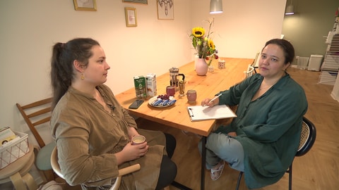 Die Hebammen Nathalie Rose (links) und Janna Hufnagel sitzen an einem Holztisch in ihrem Geburtshaus "Amma" in Aichtal: Der Bau hat den beiden viel Kraft und noch mehr Nerven abverlangt. (Foto: SWR)