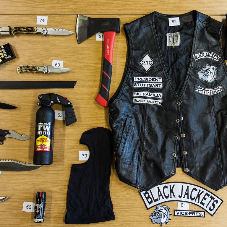 Auf einem Tisch liegen unter anderem Waffen, eine Kutte und Shirts mit Symbolen der Black Jackets. (Foto: dpa Bildfunk, picture alliance / dpa | Christoph Schmidt (Archivbild))