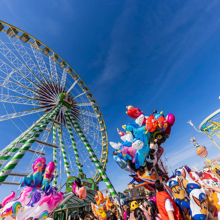 Das Datum vom Frühlingsfest 2024 in Stuttgart auf dem Wasen: 20. April bis 12. Mai. Wer ins Zelt will, sollte einen Tisch reservieren. Der Bierpreis ist gestiegen. Zu sehen sind auf dem Bild das Riesenrad, Luftballons, Menschen und die Wilde Maus. (Foto: IMAGO, IMAGO / Arnulf Hettrich)