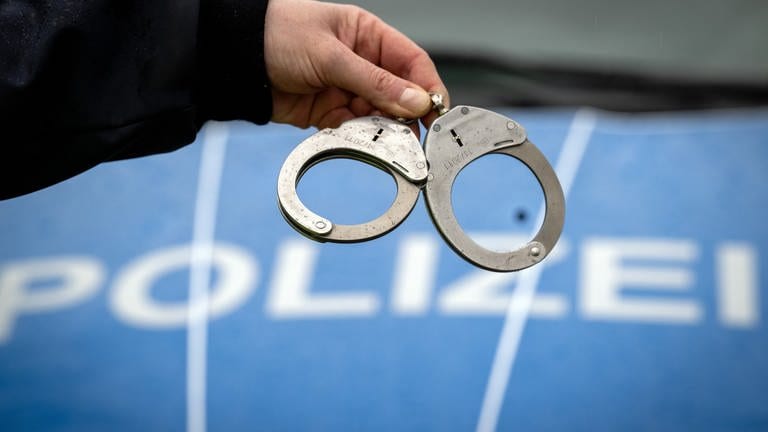 Handschellen vor einem Polizeiauto. In Stuttgart wurde ein Mann verhaftet. Er hat gestanden, seine Frau getötet zu haben. (Foto: dpa Bildfunk, picture alliance/dpa | Soeren Stache)