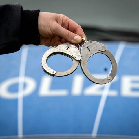 Handschellen vor einem Polizeiauto. In Stuttgart wurde ein Mann verhaftet. Er hat gestanden, seine Frau getötet zu haben. (Foto: dpa Bildfunk, picture alliance/dpa | Soeren Stache)