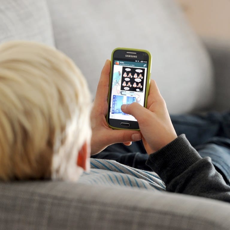 Jugendlicher liegt auf einem Sofa und blickt auf sein Smartphone. (Foto: dpa Bildfunk, Tobias Hase)