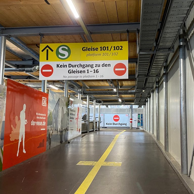 Auf dem Bild ist ein Geflecht aus Leitlinien am Boden des Stuttgarter Hauptbahnhofes und Schilder an der Decke zu sehen.