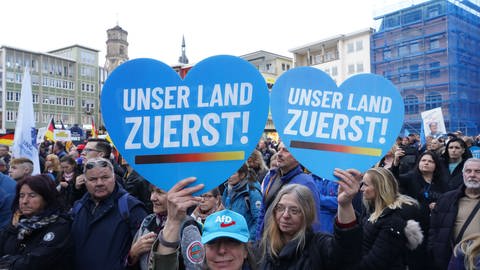 Demonstranten halten auf der AfD-Kundgebung in Stuttgart Herzen mit der Aufschrift "Unser Land zuerst" in die Kamera.