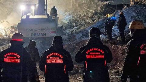 Vier Helfer stehen nachts vor den Trümmern. (Foto: Pressestelle, DeathCare Embalmingteam e.V.)