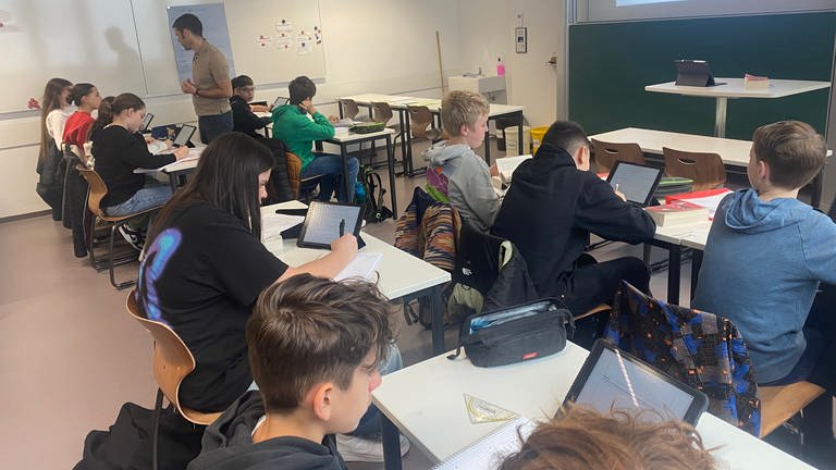 Die Schülerinnen und Schüler sitzen im Klassenzimmer und arbeiten an ihren Tablets.