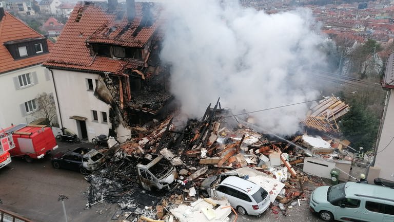 Nach der Explosion eines Doppelhauses in Stuttgart-West steht nur noch eine Haushälfte. Wo einst das Haus stand, liegen Trümmerberge, die qualmen.
