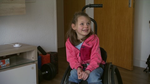 Mara ist sechs Jahre alt und hat während der Geburt zu wenig Sauerstoff bekommen. Auf dem Bild sitzt sie im Rollstuhl und lacht.