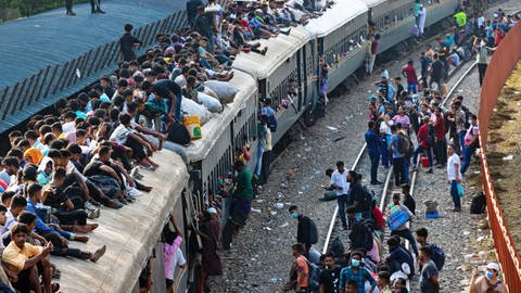 Fahrgäste, die keinen Platz im Zug haben, sitzen auf dem Dach oder laufen am Zug entlang. Eine Aufnahme aus Bangladesh. (Foto: IMAGO, IMAGO / ZUMA Wire xJoyxSahax)