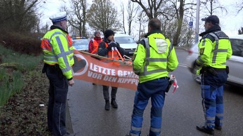 Zwei Mitglieder der "Letzten Generation" stören den Verkehr in Stuttgart. Vor ihnen stehen drei Polizisten. (Foto: Andreas Rosar)