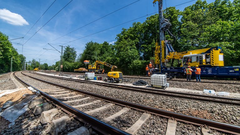 Bauarbeiter stehen im Gleisbett auf einer gesperrten Bahnstrecke in Stuttgart. Ein paar von ihnen bedienen große Baumaschinen. (Foto: dpa Bildfunk, picture alliance/dpa | Christoph Schmidt)
