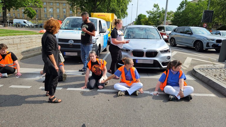 Klimaaktivsten sitzen auf der Straße, dahinter stehende Autos