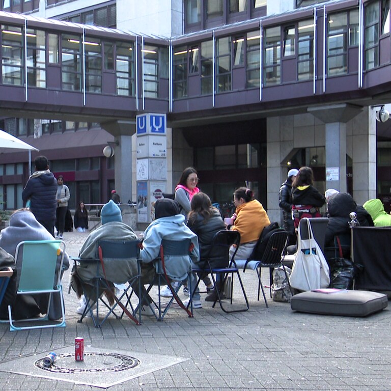 Menschen mit Stühlen und Kissen vor Bürgerbüro und Ausländerbehörde in Stuttgart.