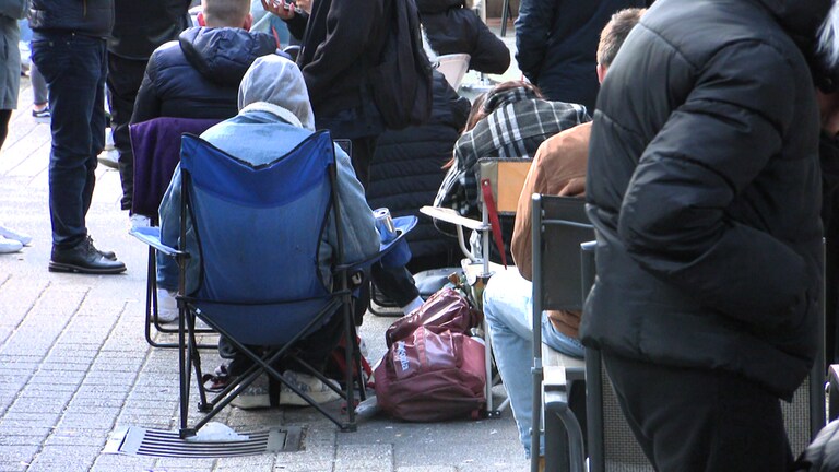 Menschen sitzen auf Stühlen und stehen in der Schlange vor der Ausländerbehörde Stuttgart.