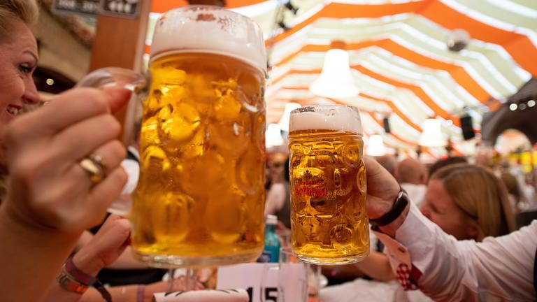 In einem Festzelt auf dem Cannstatter Volksfest halten stoßen mehrere Menschen an einem Tisch mit Bierkrügen an.