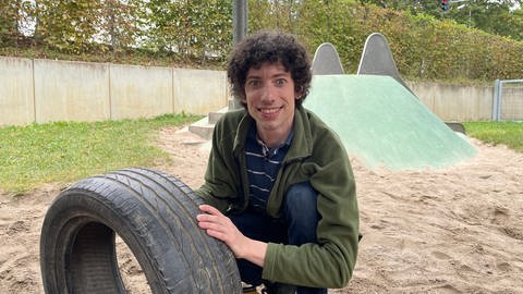 Quereinsteiger Florian Treßelt hält in einem Sandkasten einen Reifen in der Hand. Er war mal Schreiner und wird jetzt Kita-Mitarbeiter.