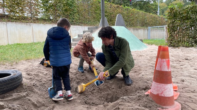 Florian Treßelt sitzt in einem Sandkasten mit Kindern. Der 35-Jährige lässt sich gerade zum Pädagogen umschulen.