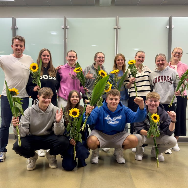 Schülerinnen und Schüler zusammen mit ihren Lehrkräften halten Sonnenblumen hoch. Sie sind kurz zuvor auf dem Flughafen Stuttgart angekommen. (Foto: privat: Jens Kaiser)