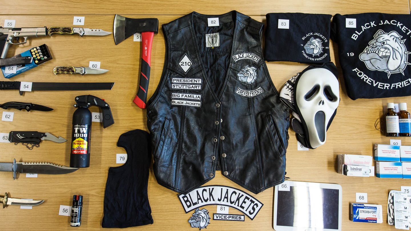 Auf einem Tisch liegen unter anderem Waffen, eine Kutte und Shirts mit Symbolen der Black Jackets. (Foto: dpa Bildfunk, picture alliance / dpa | Christoph Schmidt (Archivbild))