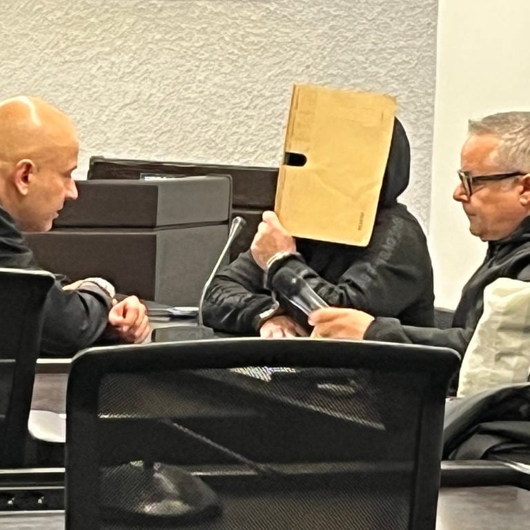 Der Angeklagte hält einen beige-farbenen Ordner vor sein Gesicht - beim Prozessauftakt im Landgericht Stuttgart. (Foto: SWR, Werner Trefz)