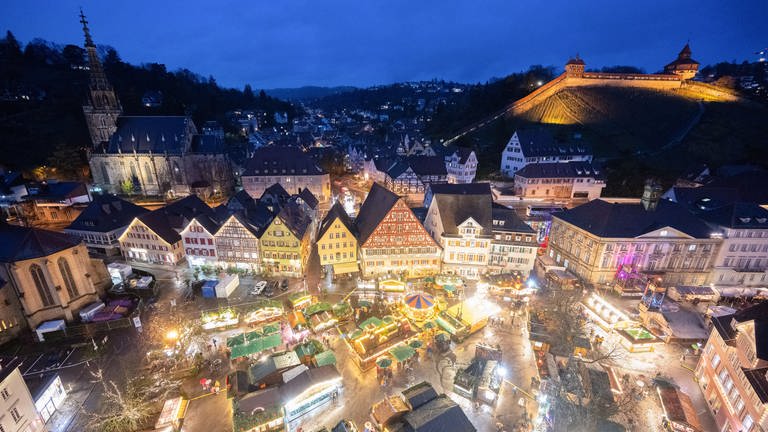 Die Stände des Weihnachtsmarkts Esslingen leuchten am Abend. Im Hintergrund die Esslinger Burg.