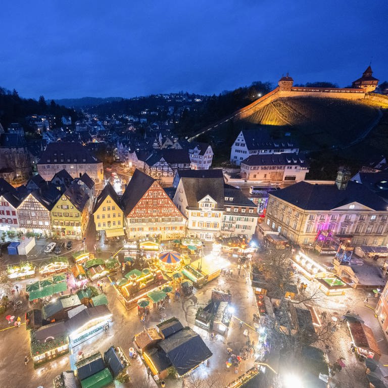 Die Stände des Weihnachtsmarkts Esslingen leuchten am Abend. Im Hintergrund die Esslinger Burg.