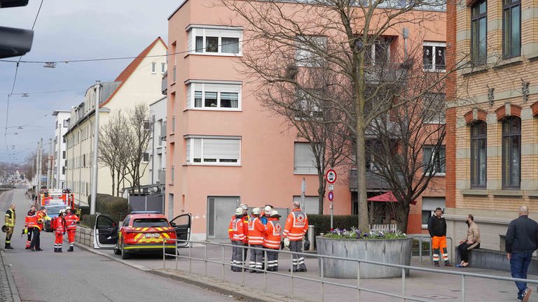 Mehrere Einsatzkräfte der Feuerwehr und Polizei sthene vor einem Mehrfamilienhaus in Stuttgart.