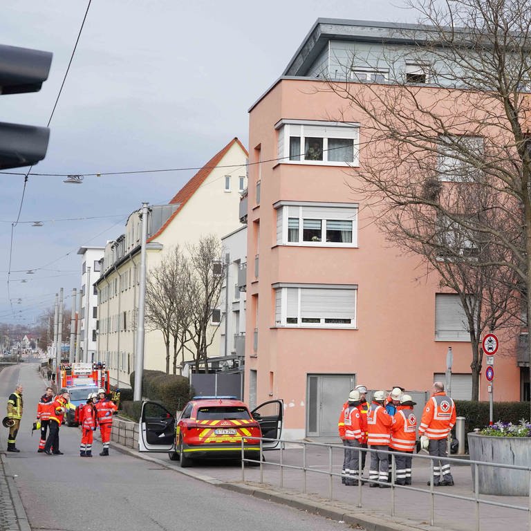 Mehrere Einsatzkräfte der Feuerwehr und Polizei sthene vor einem Mehrfamilienhaus in Stuttgart.