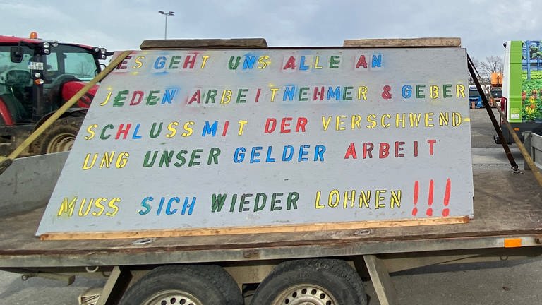 Ein Protestierender auf dem Wasen in Stuttgart hat sein Plakat auf einen Anhänger geladen: Landwirtinnen und Landwirte aus ganz Baden-Württemberg demonstrieren auf dem Cannstatter Wasen in Stuttgart. (Foto: SWR, Diana Hörger)