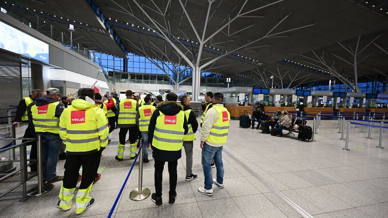 Streikende Mitarbeiter des Flughafens Stuttgart stehen am 17. März 2023 mit Westen der Gewerkschaft ver.di in der leeren Abflughalle.
