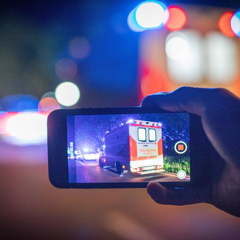 Auf einem Handy-Display sieht man einen Krankenwagen bei Nacht. Symbolbild für Gaffer an Unfallort. (Foto: IMAGO, xMarcxGruberx)