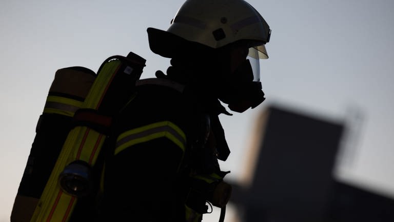 Ein Feuerwehrmann in Atemschutzausrüstung steht an einem Einsatzfahrzeug der Feuerwehr. Ein Kind soll in einem Auto Feuerwerk angezündet und dadurch einen Brand auf der Autobahn 8 bei Stuttgart verursacht haben, teilt die Polizei mit.