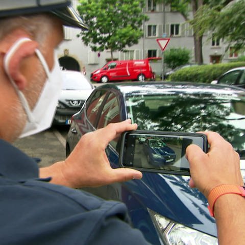 Ein Mitarbeiter des Ordnungsamtes macht mit dem Handy ein Foto von parkendem Auto auf Gehweg  (Foto: SWR)