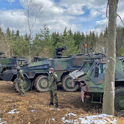 Große Bundeswehrfahrzeuge stehen auf einer freien Fläche im Wald. Davor stehen Soldaten. (Foto: SWR, Thorben Langwald)