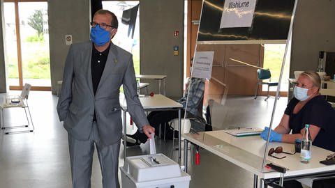 Klaus Eberhardt wirft seinen Stimmzettel in eine Wahlurne. Er trägt einen Mundschutz. (Foto: SWR, Matthias Zeller)