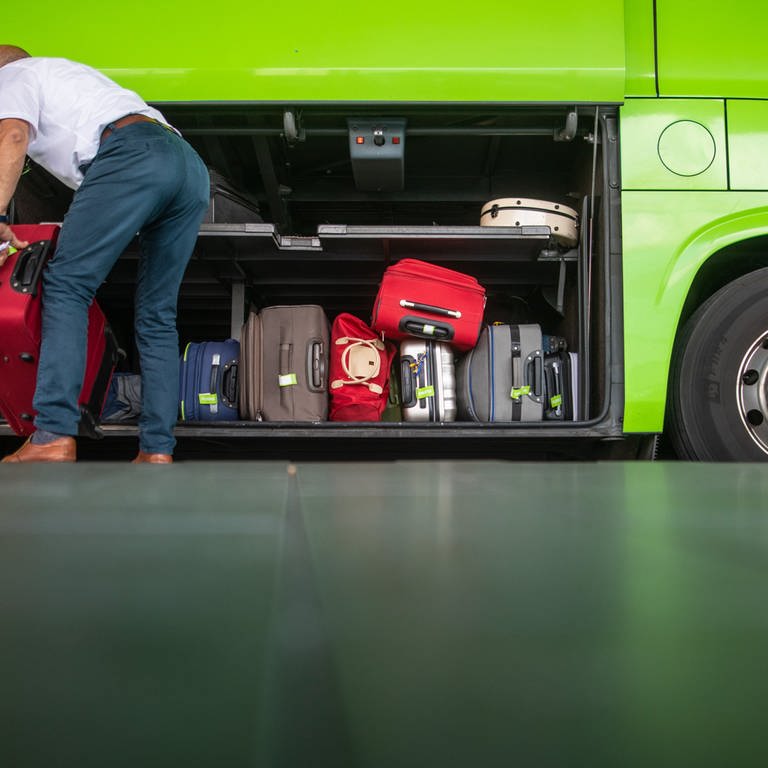 ein Mann räumt Gepäckstücke in einen grünen Bus (Foto: picture-alliance / Reportdienste, dpa Bildfunk, Christoph Schmidt)
