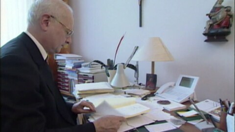 Ex-Erzbischof Robert Zollitsch sitzt an einem Schreibtisch in einem Büro. (Foto: SWR)