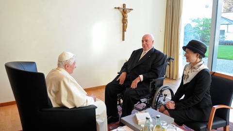 Papst sitzt gegenüber von einem älteren Mann mit weißen Haaren und Anzug. Neben ihm sitzt eine Frau mit Hut.  (Foto: picture alliance / dpa / Guido Bergmann)