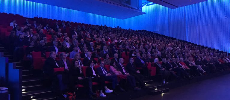 Viele Menschen sitzen auf roten Stühlen und verfolgen eine Ansprache. (Foto: SWR, Ulf Seefeld)
