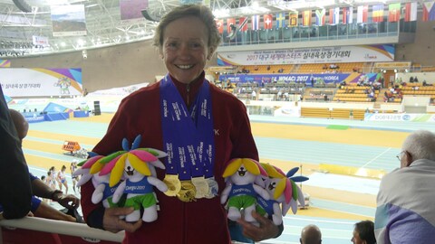 Brigitte Nidel hat vier Medaillen umgehängt und mehrere Blumensträuße und kleine Plüschmaskottchen auf dem Arm. (Foto: SWR)