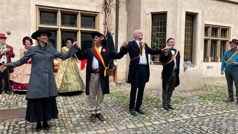 Kostümierte Darsteller in Freiburg halten einander an den Händen. (Foto: SWR)