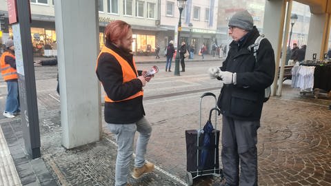 Ein junger Mann mit Warnweste unterhält sich mit einem älteren Mann in der Fußgängerzone. (Foto: SWR)