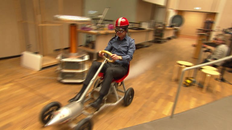 Ausgestattet mit Helm und Motorradbrille - so fährt Professor Fischer auf seinem Raketen-Go-Kart mit CO2-Antrieb durch den Hörsaal.  (Foto: SWR, Stefan Troendle)