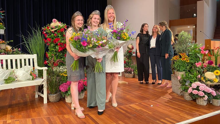 Drei junge Frauen mit Kronen und Blumensträußen stehen auf einer Bühne. (Foto: SWR)