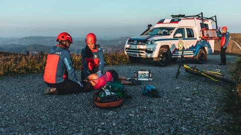 Mehrere Retter der Bergwacht sind im Einsatz. Sie tragen rote Helme und blaue Jacken. Im Hintergrund ist die malerische Kulisse des Schwarzwaldes zu sehen. (Foto: Bergwacht Schwarzwald e.V.)