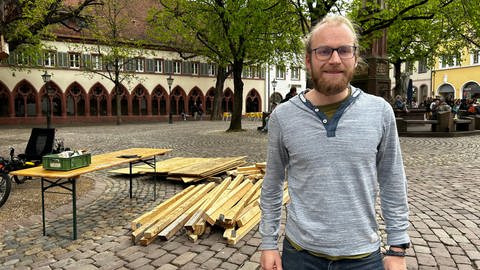 Vor dem Freiburger Rathaus liegen bereits Holzlatten auf dem Platz. Aus einem Kleinlaster laden Menschen weiteres Material.